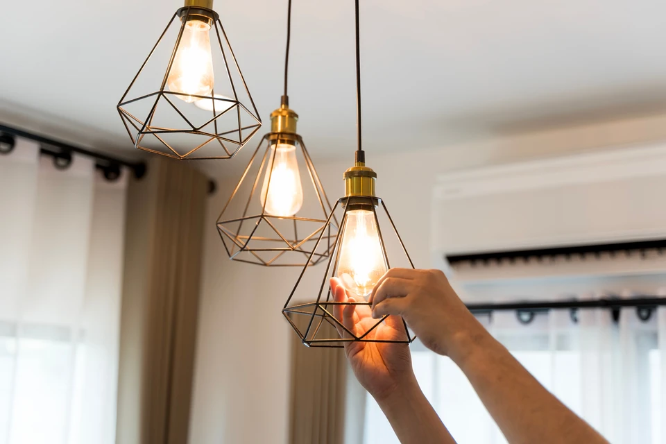 Ouvrier en bâtiment installant un luminaire suspendu dans un intérieur moderne