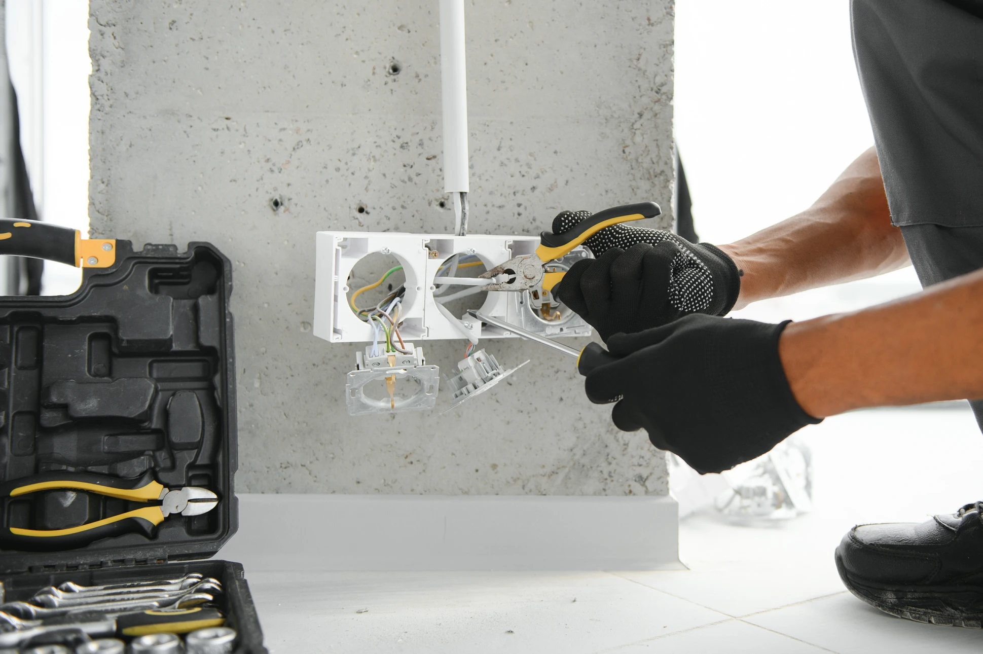 Électricien professionnel en gants de protection travaillant sur installation électrique murale