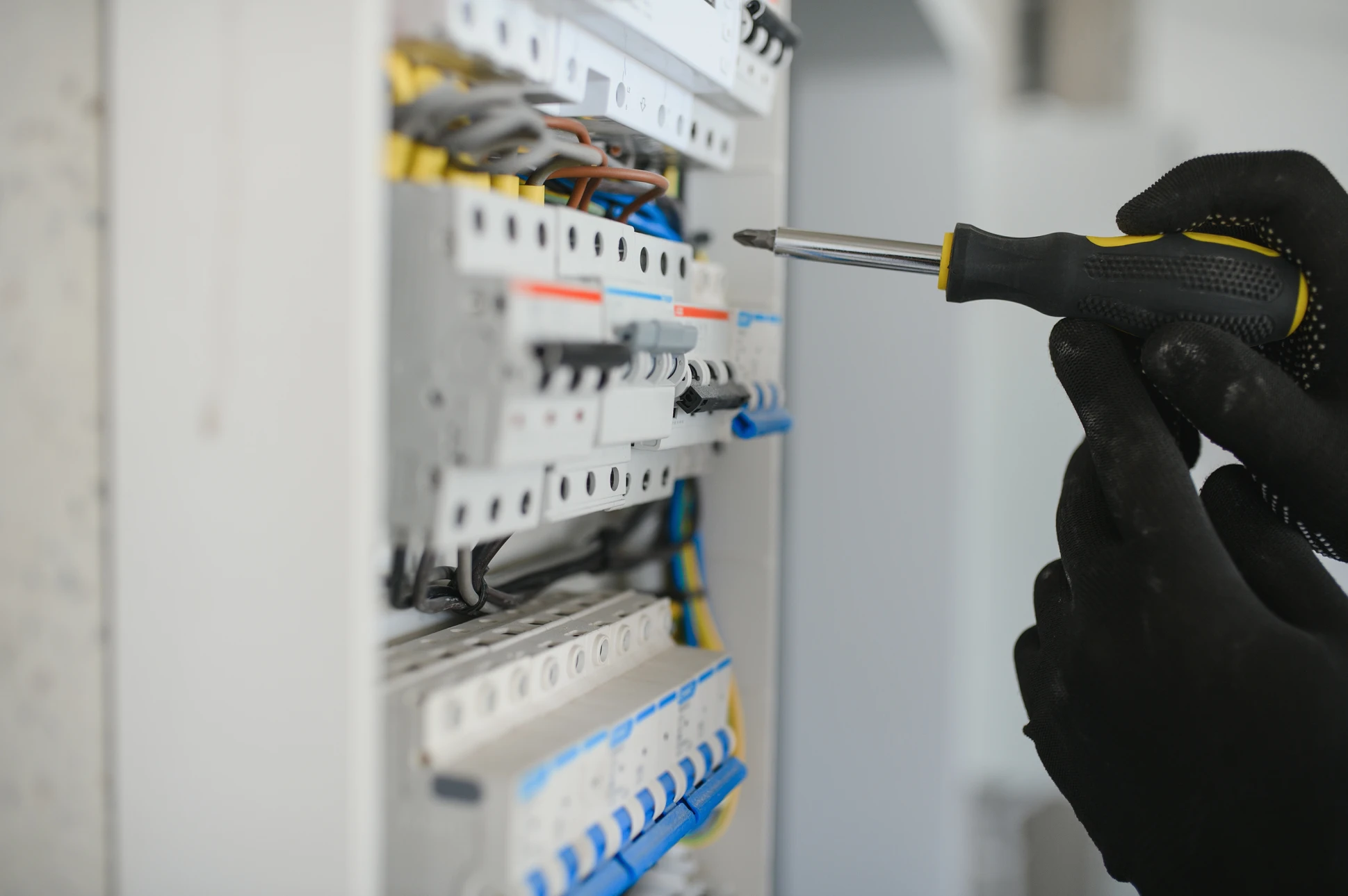 Électricien professionnel en salopette bleue et casque jaune dans cuisine moderne, portant câbles électriques et caisse à outils
