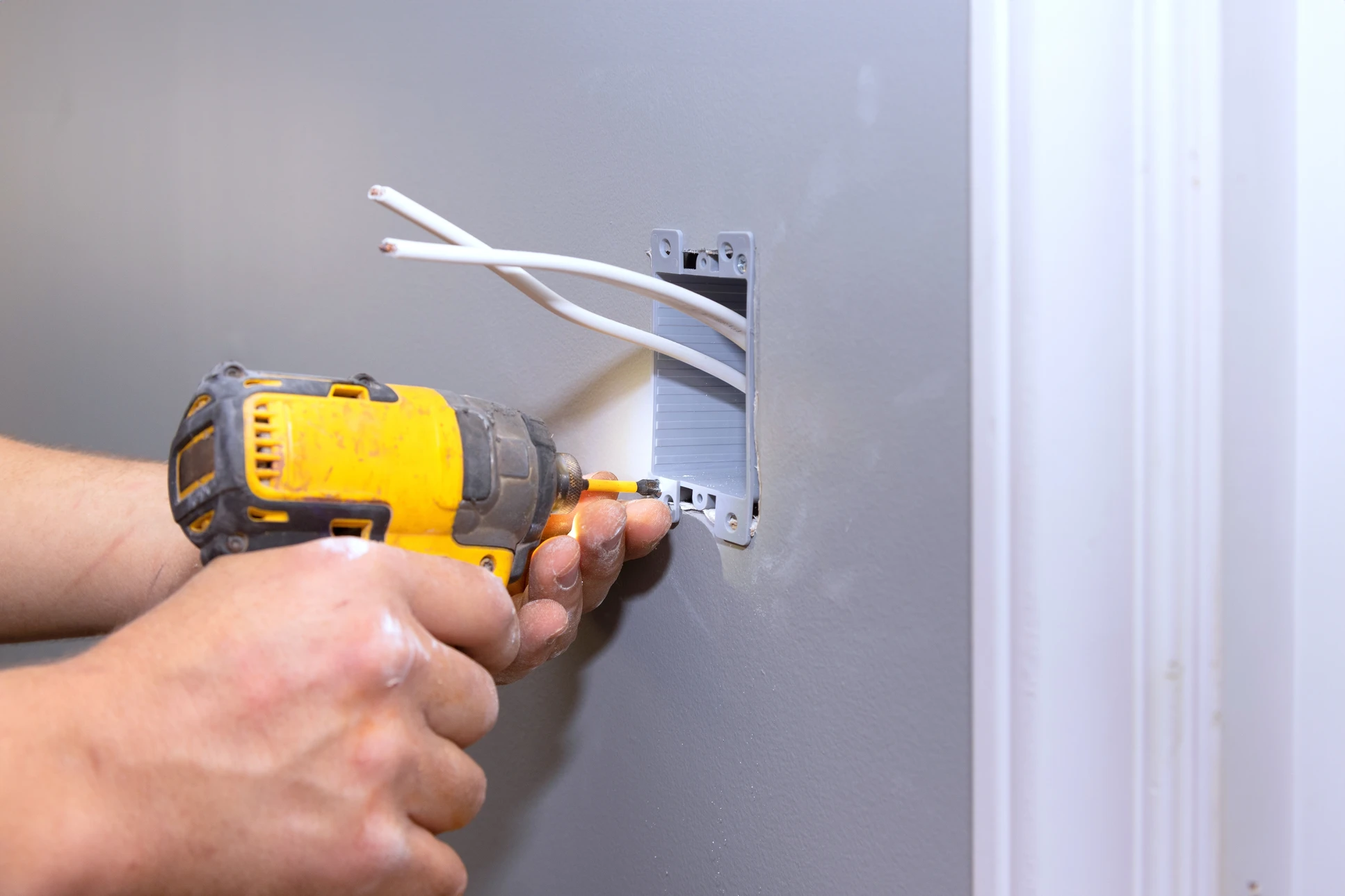 Intérieur domestique, mains d'électricien utilisant une pince à dénuder sur câbles électriques près d'un boîtier d'encastrement bleu fixé au mur blanc