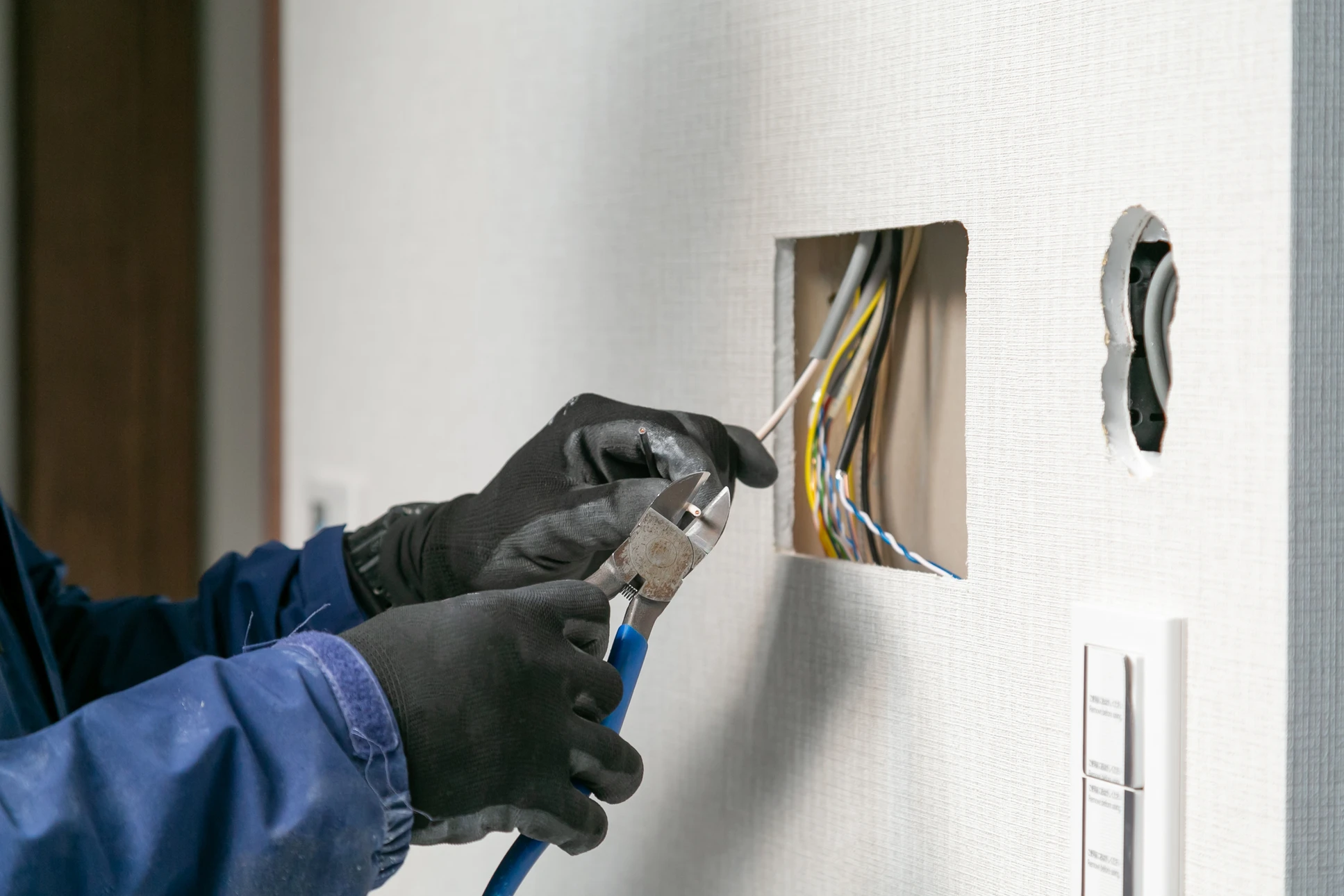 Photographie d'un électricien qualifié en tenue professionnelle (vêtements de travail, gilet de sécurité) effectuant une intervention d'installation ou de mise aux normes électrique dans un intérieur résidentiel. L'électricien est en action (manipulation de câbles, installation d'éléments électriques ou diagnostic) dans un logement bordelais typique. La scène transmet professionnalisme, compétence technique et sécurité, illustrant directement le service d'installation électrique qualifiée proposé.